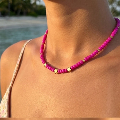 Person wearing a pink beaded necklace with star charms on a beach.