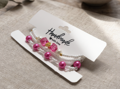 Set of pearl and pink bead hair ties on a white card with 'Handmade with Love' text, placed on a textured beige surface.