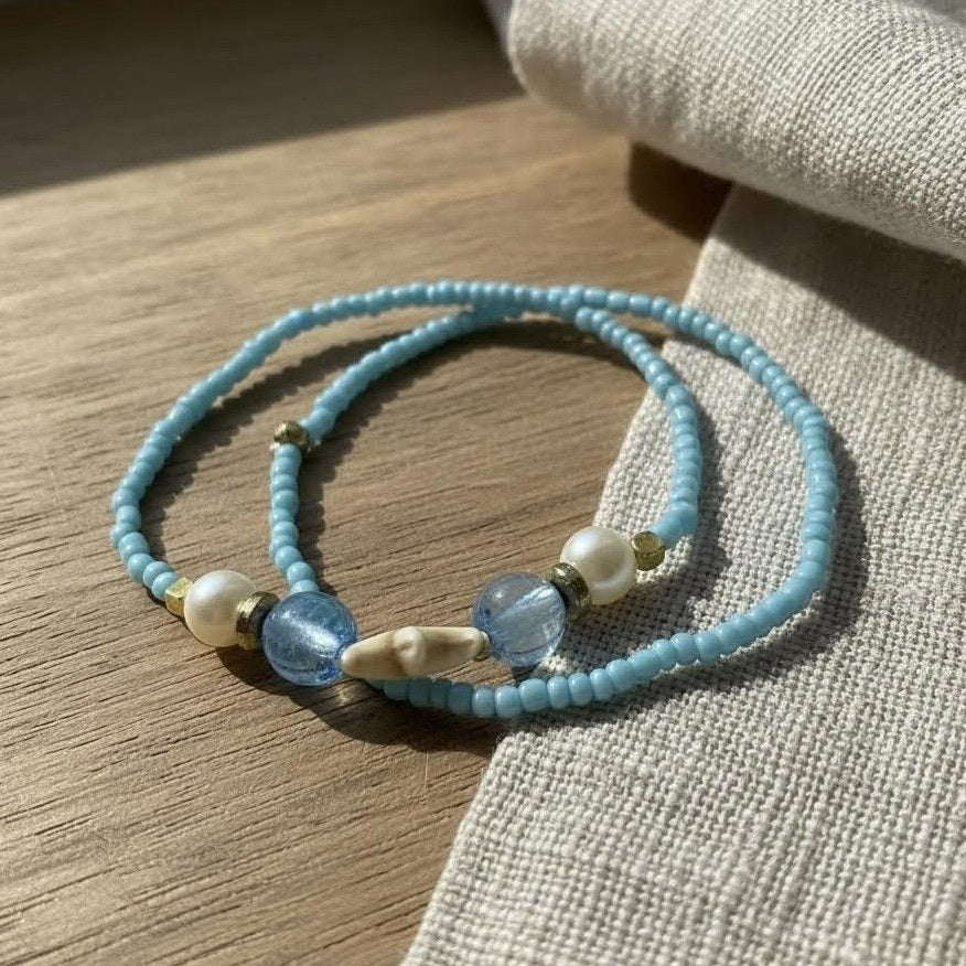 Light blue beaded bracelet with pearls and gold accents on a wooden surface