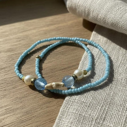 Light blue beaded bracelet with pearls and gold accents on a wooden surface