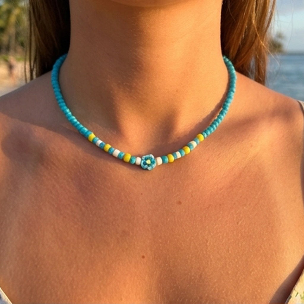 Close-up of a turquoise beaded necklace with a flower pendant on a person by the water.