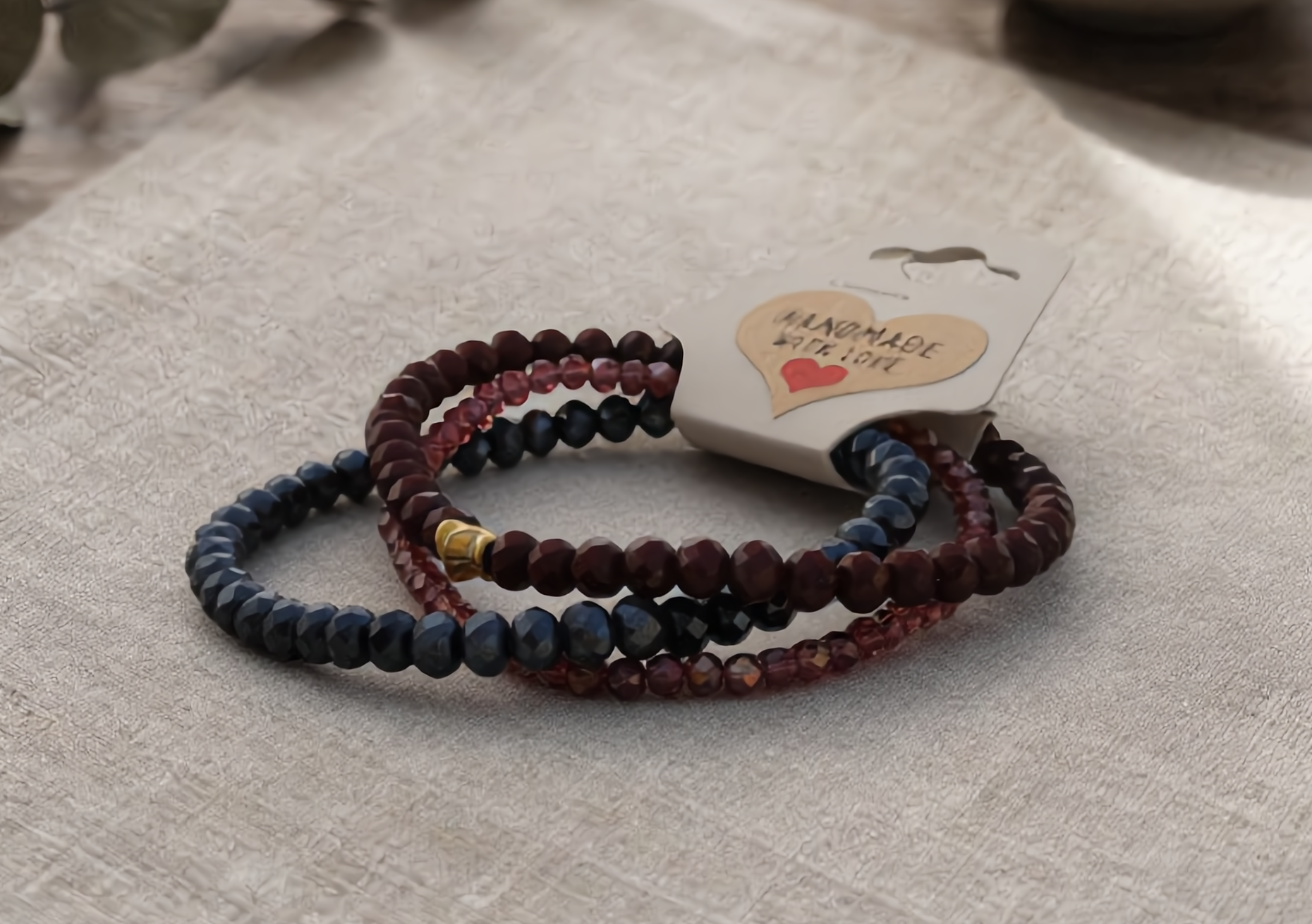 Set of beaded bracelets on a textured surface with a 'Handmade with Love' tag.