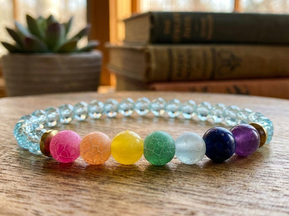 Colorful beaded bracelet on a wooden surface with books and a plant in the background