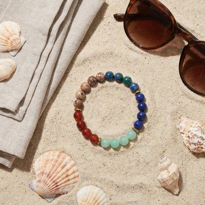 Colorful beaded bracelet on sand with shells and sunglasses