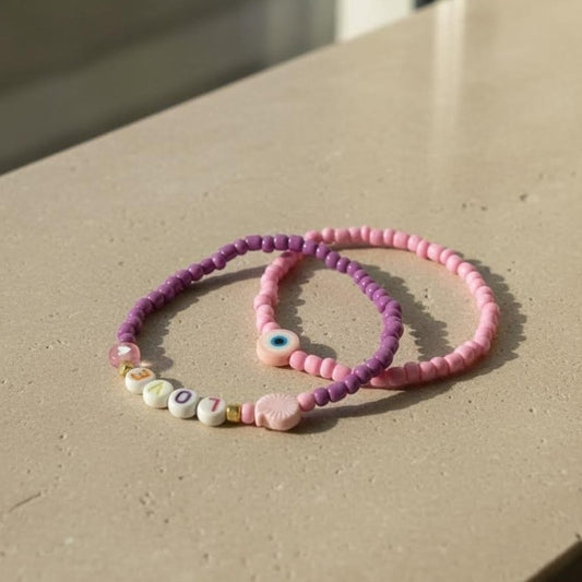 Two beaded bracelets, one purple and one pink, on a light surface.