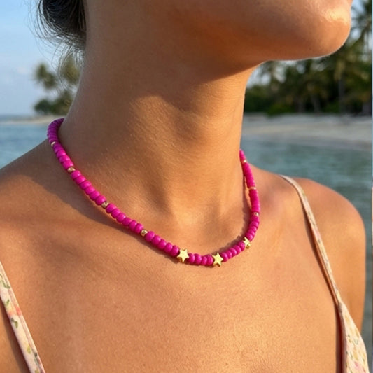 Person wearing a pink beaded necklace with a blurred beach background