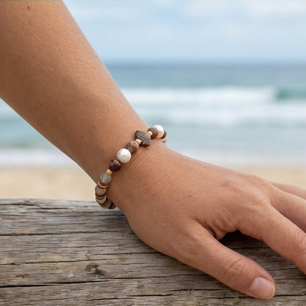 Hand wearing a beaded bracelet with a blurred beach background