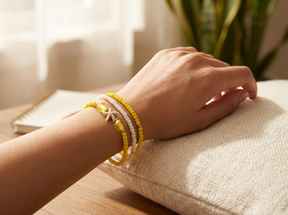 Hand wearing a yellow bracelet on a cushion with a plant in the background