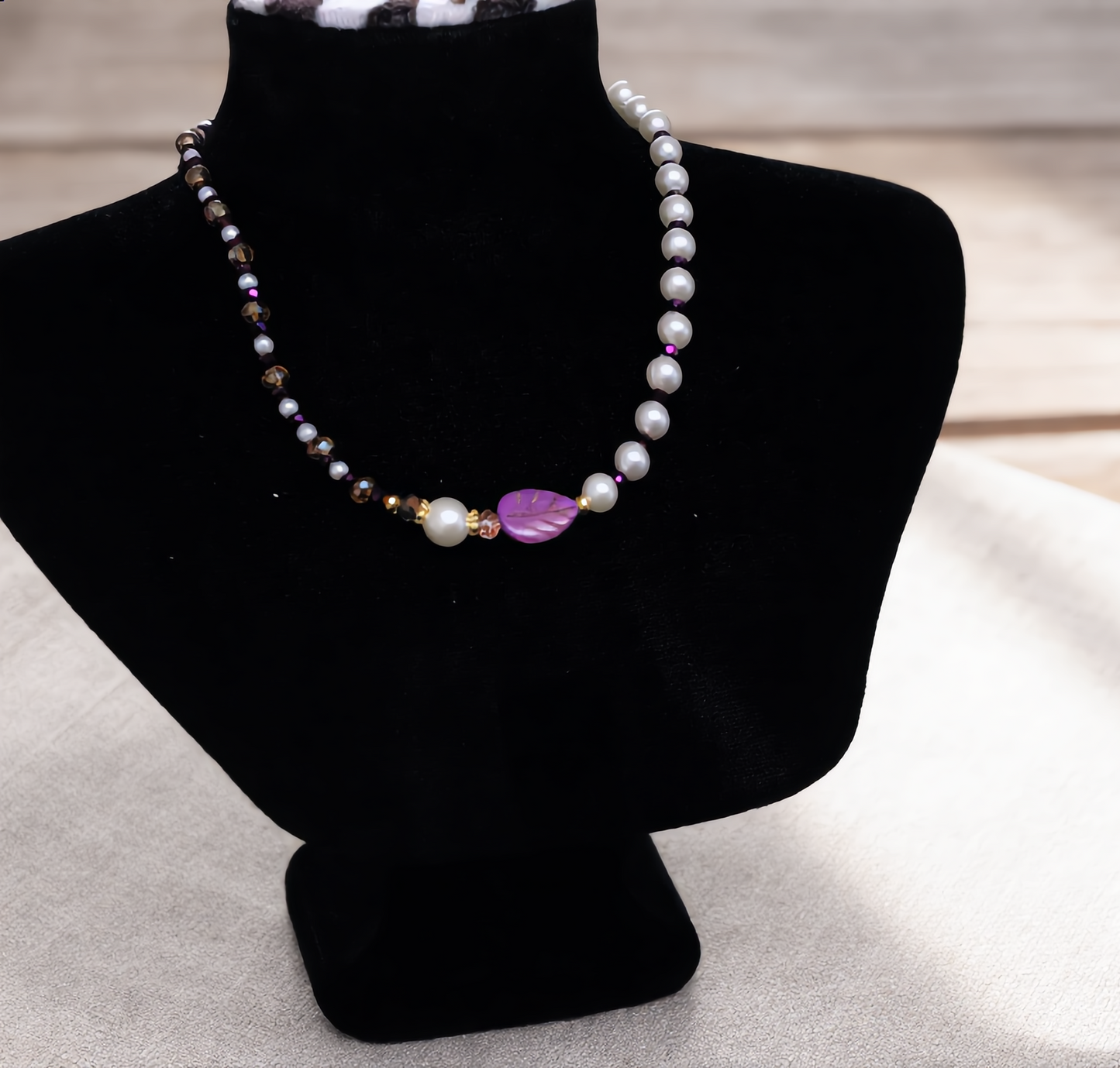 Pearl necklace with a purple heart pendant on a black mannequin bust.