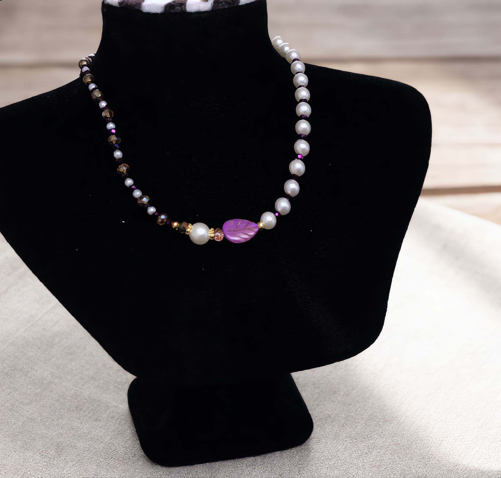 Pearl necklace with a purple heart pendant on a black mannequin bust.