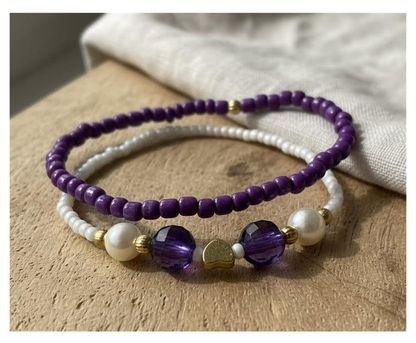 Two beaded bracelets with purple and white beads on a wooden surface.
