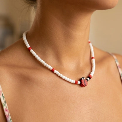 Close-up of a person wearing a red and white beaded necklace with a blurred background