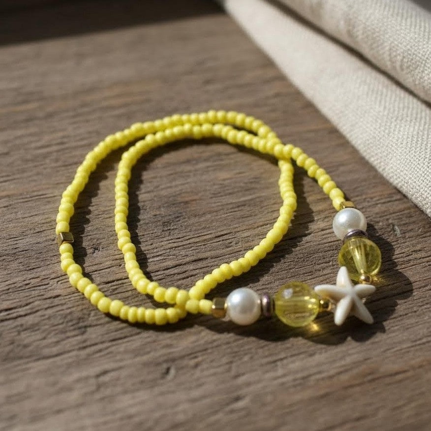 Yellow beaded bracelet with white starfish charm on a wooden surface