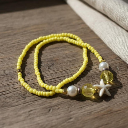 Yellow beaded bracelet with white starfish charm on a wooden surface