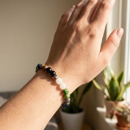 Hand wearing a beaded bracelet with plants in the background