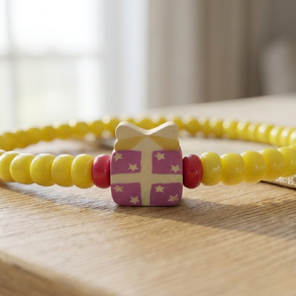 Yellow beaded bracelet with a decorative purple charm on a wooden surface