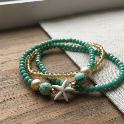 Set of green beaded bracelets with gold accents and a starfish charm on a wooden surface.