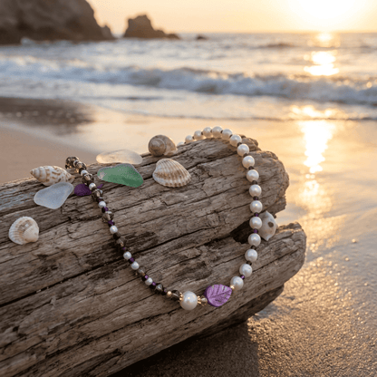 Pearl bracelet with decorative elements on a piece of driftwood by the beach at sunset.