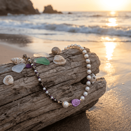Pearl bracelet with decorative elements on a piece of driftwood by the beach at sunset.