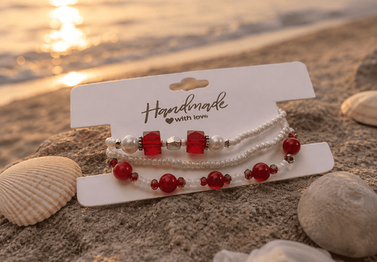 Set of beaded bracelets on a card with 'Handmade with Love' text, placed on sand with a sunset background.