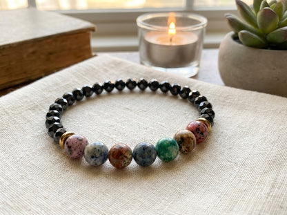 Multicolored beaded bracelet on a textured surface with a candle and plant in the background