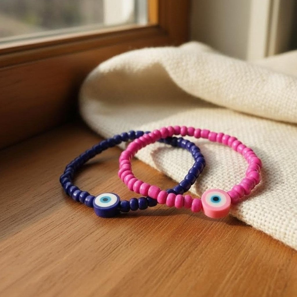 Two beaded bracelets, one pink and one blue, on a wooden surface with a soft fabric background.