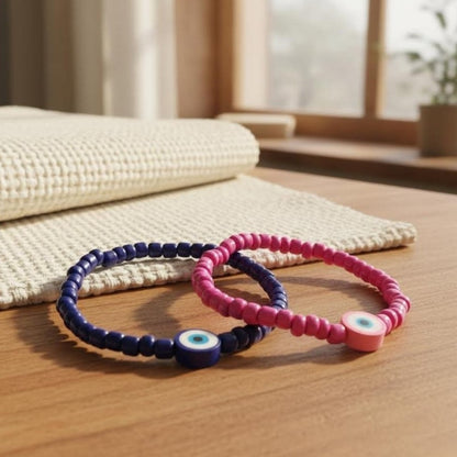 Two beaded bracelets, one pink and one blue, on a wooden surface with a blurred indoor background.