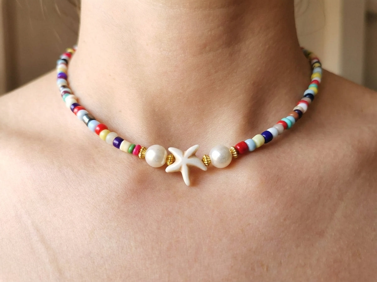Colorful beaded necklace with starfish and pearl charm on a person's neck.