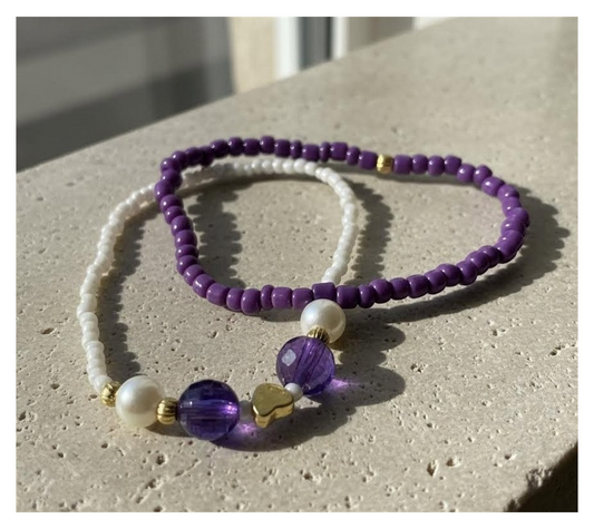 Two beaded necklaces, one purple and one white with purple accents, on a textured surface.