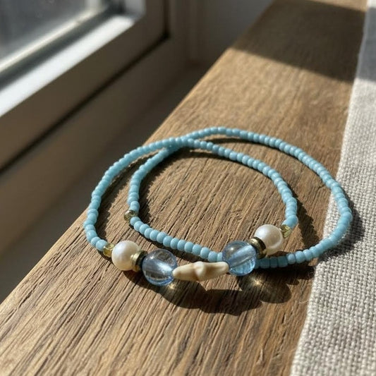 Two blue beaded bracelets with pearls on a wooden surface.