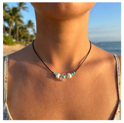 Necklace with turquoise and white beads worn by a person on a beach.
