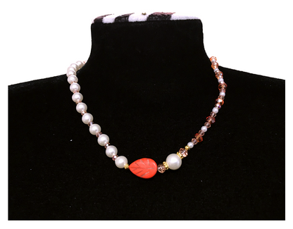 Necklace with pearls and a red leaf-shaped bead on a black mannequin.