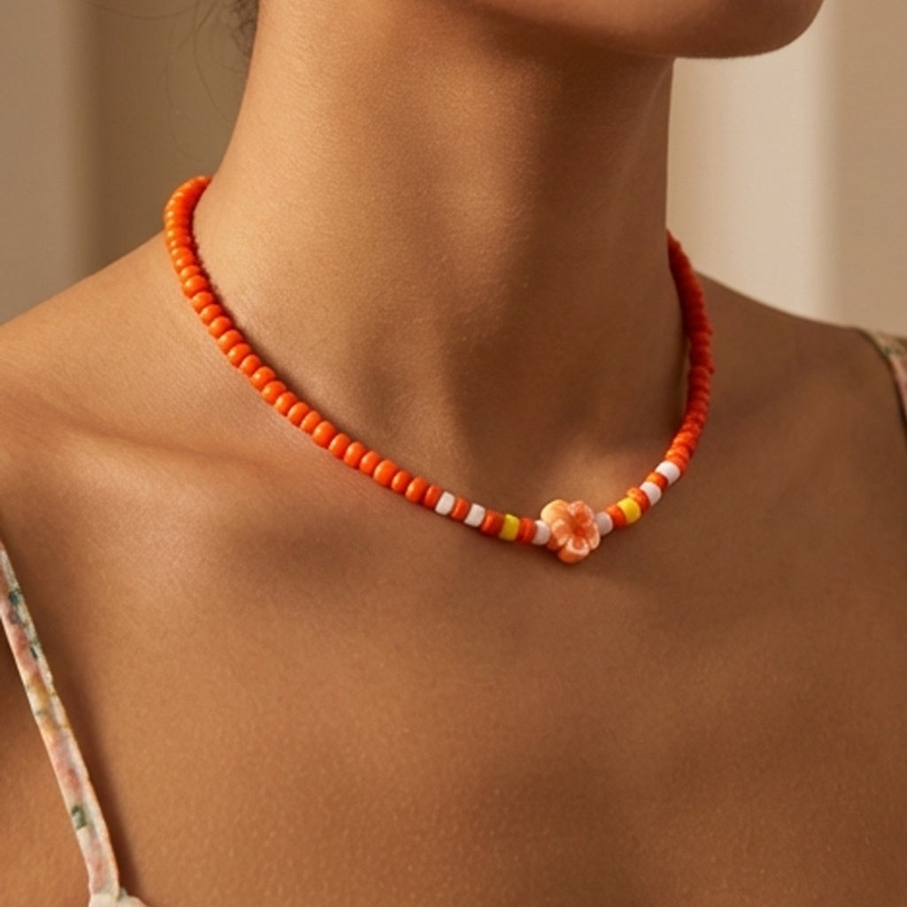 Necklace with orange beads and a floral charm on a person's neck against a neutral background