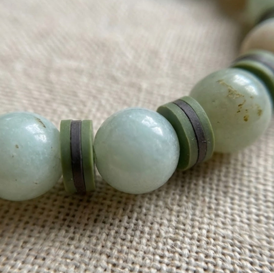 Close-up of a green beaded bracelet on a textured fabric background
