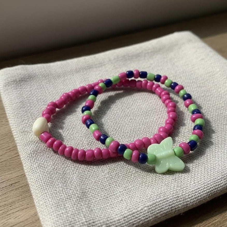 Two colorful beaded bracelets with a butterfly charm on a textured surface.