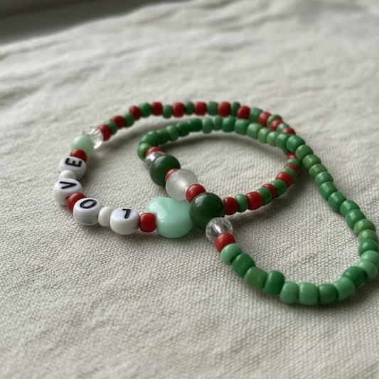 Beaded necklace with green, red, and white beads on a textured fabric background