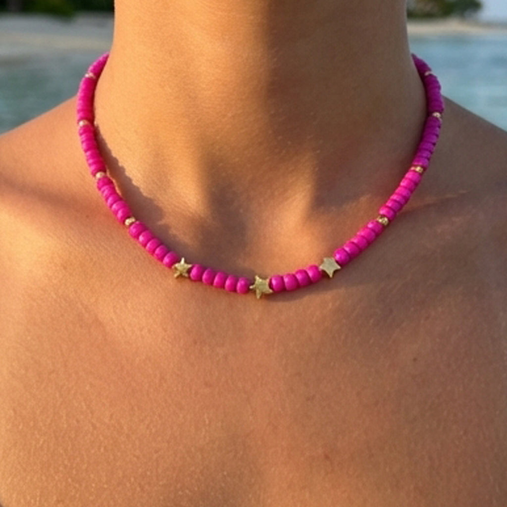 Pink beaded necklace with gold stars worn by a person by a body of water.