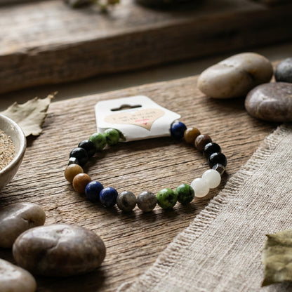 Stones bracelet on a wooden surface with pebbles and a card in the background