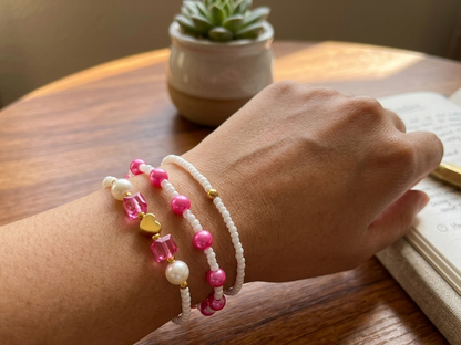 Hand wearing two beaded bracelets on a wooden surface with a plant in the background