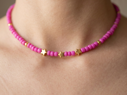 Pink beaded necklace with gold star accents on a person's neck