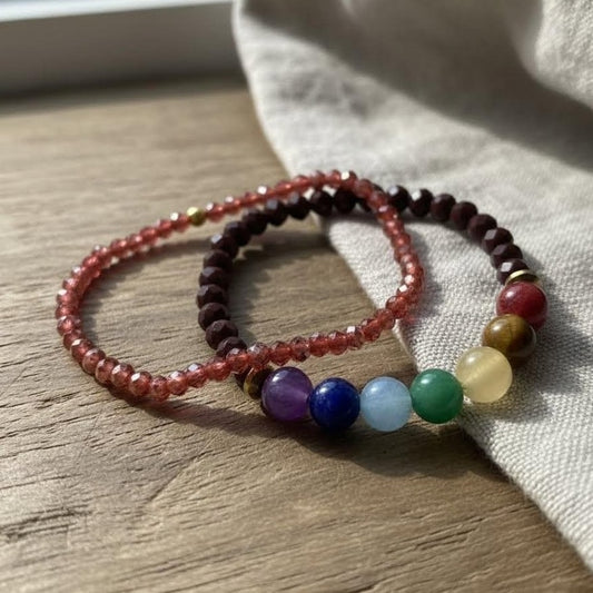 Two beaded bracelets on a wooden surface with a white fabric background
