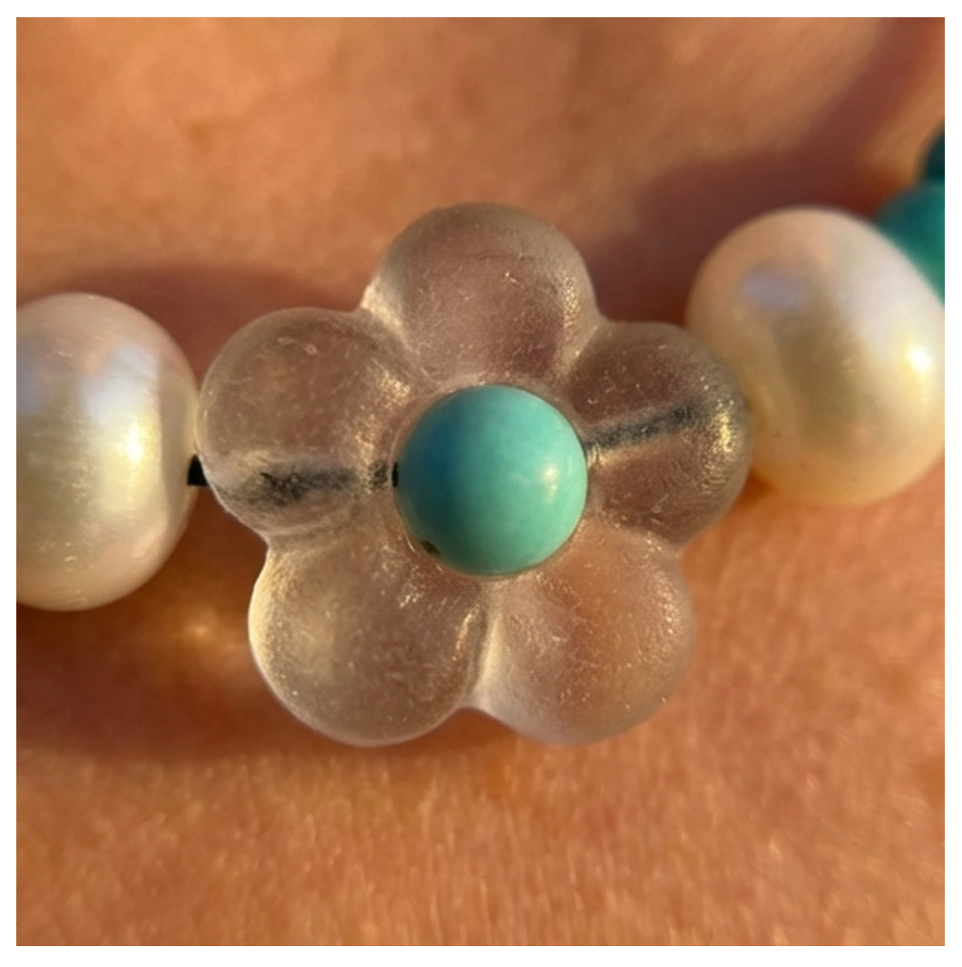 Close-up of a bracelet with a clear flower-shaped bead and turquoise center on a skin background