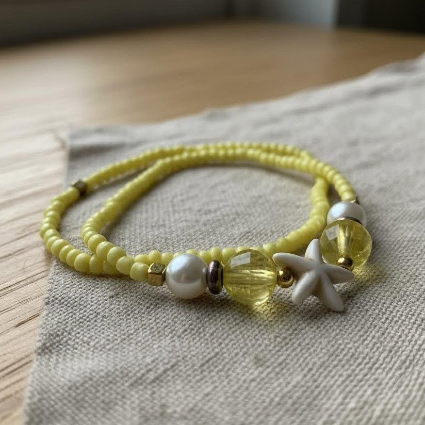 Yellow beaded bracelet with starfish charm on a textured fabric surface