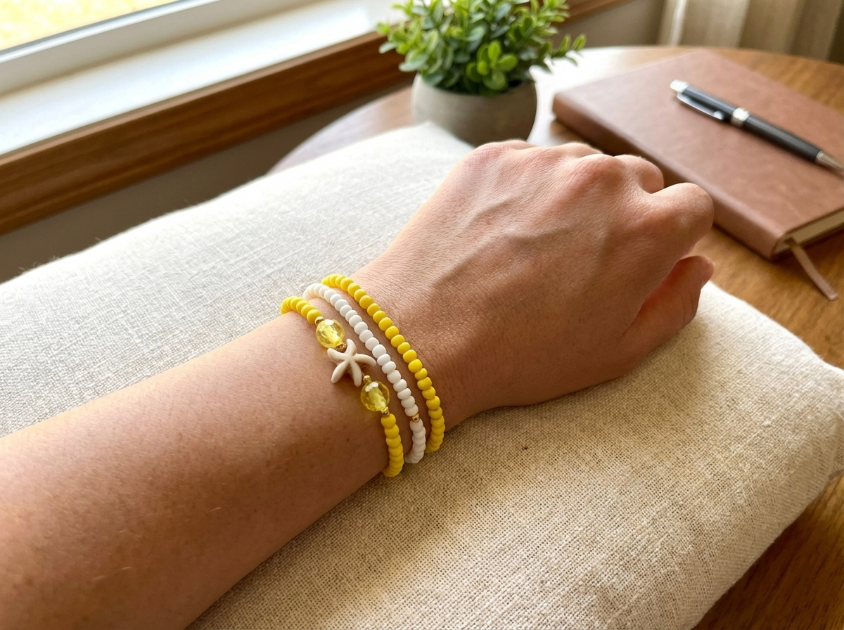 Hand wearing a yellow bracelet on a cushioned surface with a notebook and pen in the background