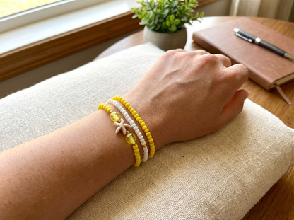 Hand wearing a yellow bracelet on a cushioned surface with a notebook and pen in the background