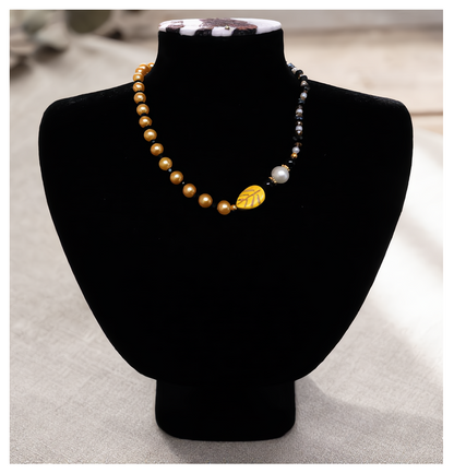 Pearl necklace with a gold leaf pendant on a black mannequin bust.