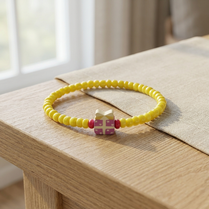 Yellow beaded bracelet with a pink and white charm on a wooden surface.