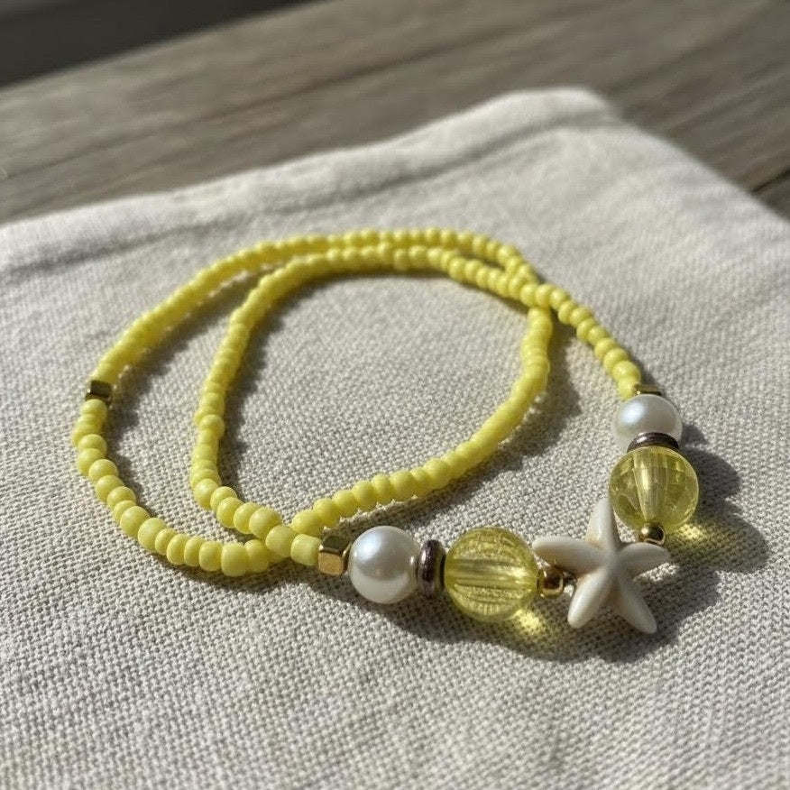 Yellow beaded bracelet with white starfish charm on a textured fabric background