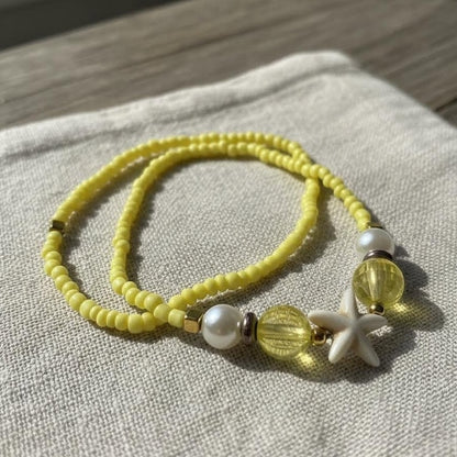 Yellow beaded bracelet with white starfish charm on a textured fabric background