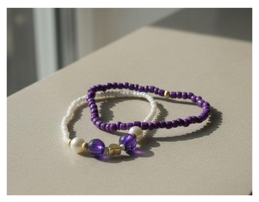 Two beaded bracelets, one white and one purple, on a light surface.